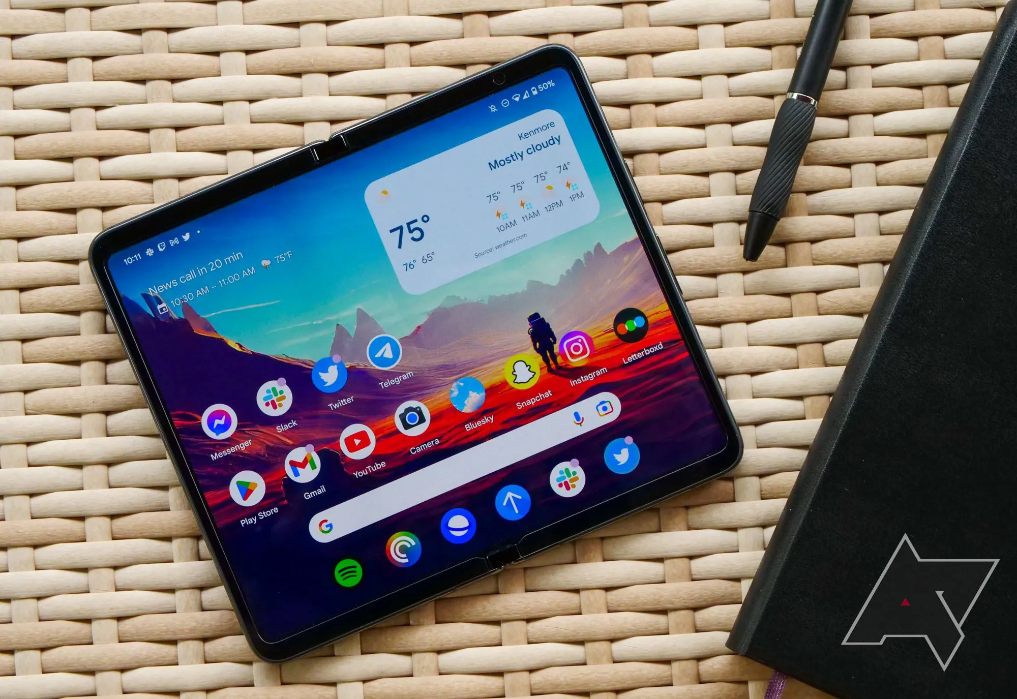 Điện thoại gập Google Pixel Fold đặt trên bàn mây cùng sổ và bút