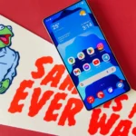 Điện thoại Samsung Galaxy S25 Ultra hiển thị màn hình chính, đặt trên cờ hiệu ghi chữ