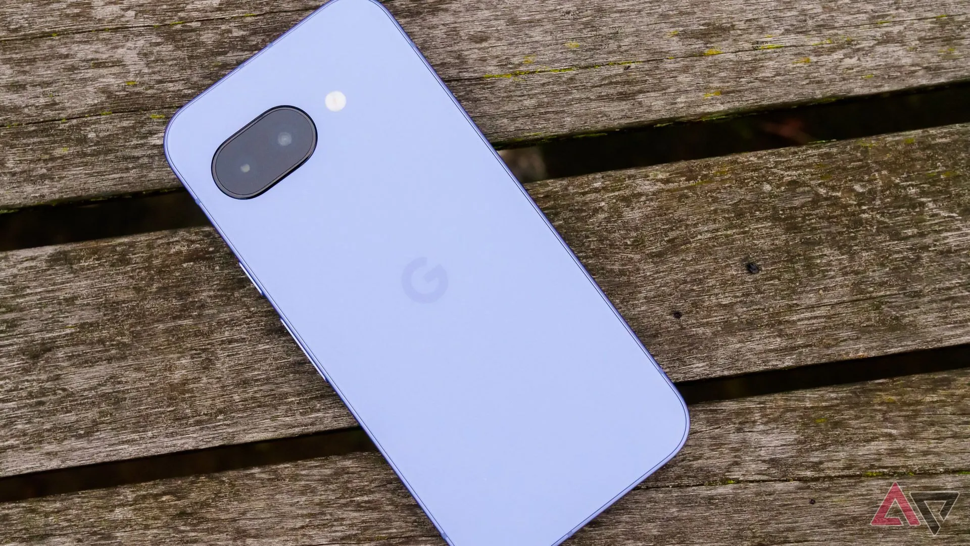 Mặt lưng điện thoại Google Pixel 9a đặt trên ghế gỗ trong công viên.