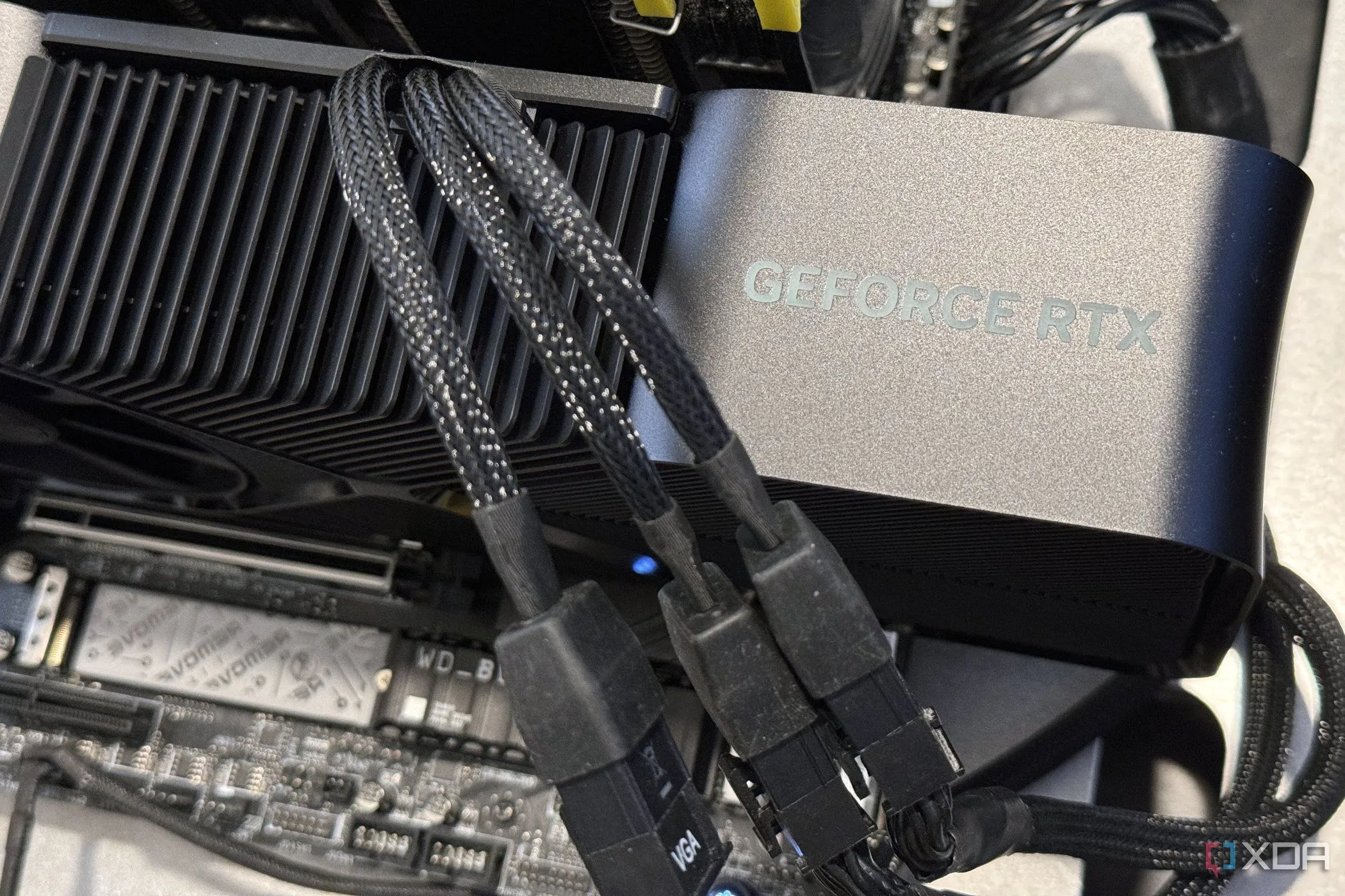 Card đồ họa NVIDIA GeForce RTX 4080 SUPER Founders Edition với ba cáp nguồn cắm vào bộ chuyển đổi, minh họa cho mức tiêu thụ điện năng thấp hơn của dòng RTX 40.