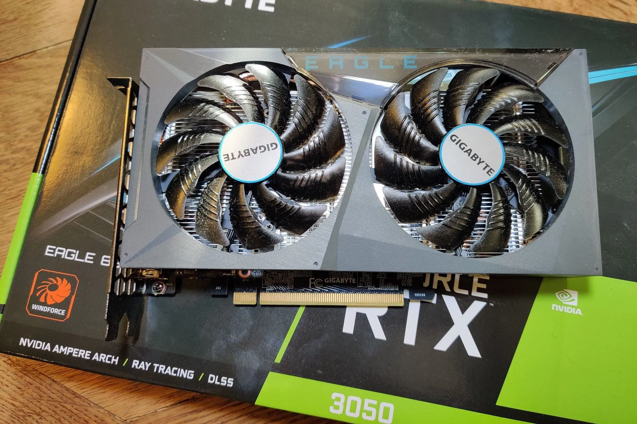 Card đồ họa NVIDIA RTX 3050 màu xám với hai quạt làm mát, đặt trên hộp bán lẻ, biểu tượng cho card tầm trung