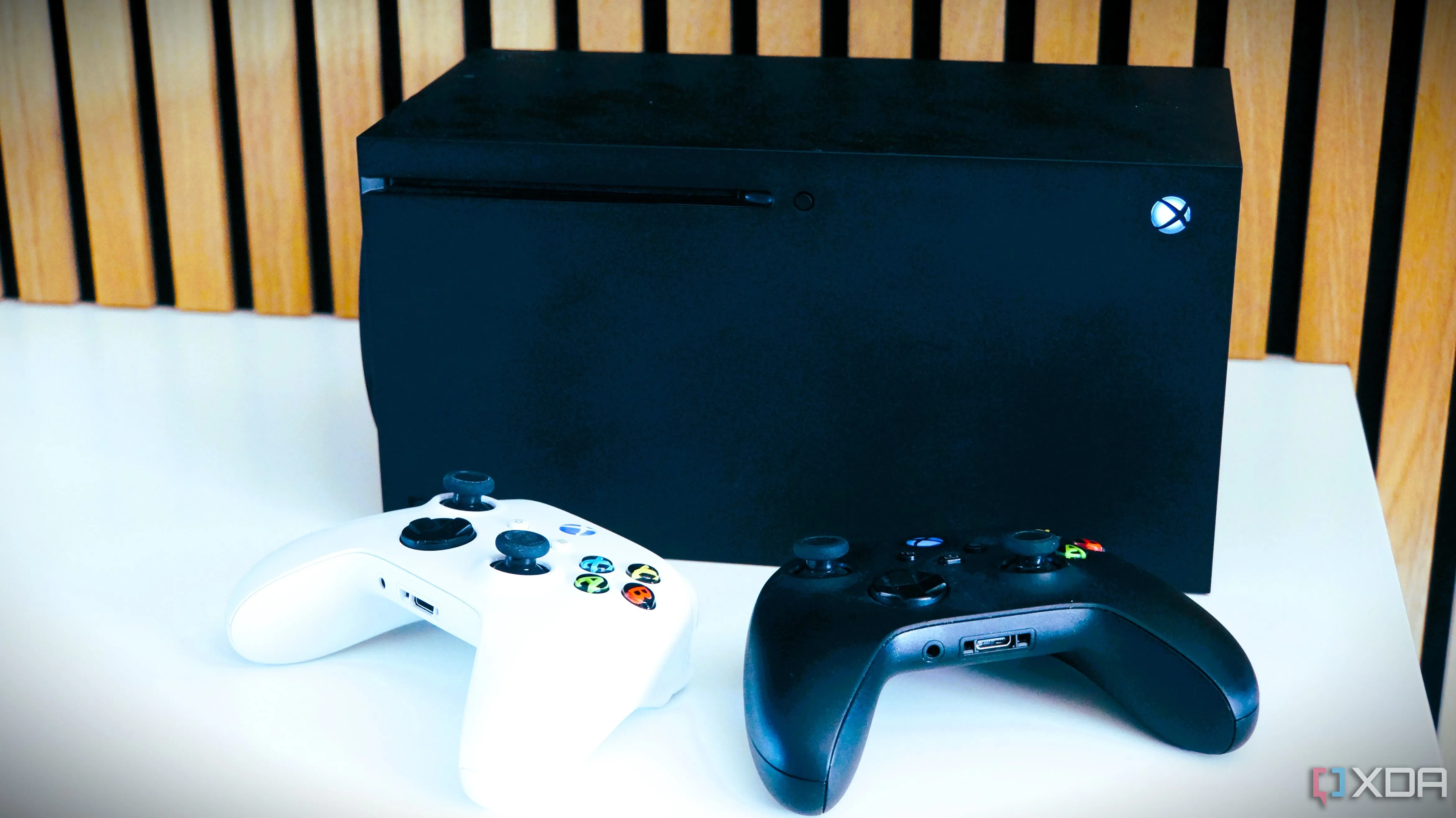 Hai bộ điều khiển Xbox trước máy console Xbox Series X, minh họa cho việc tăng giá phần cứng