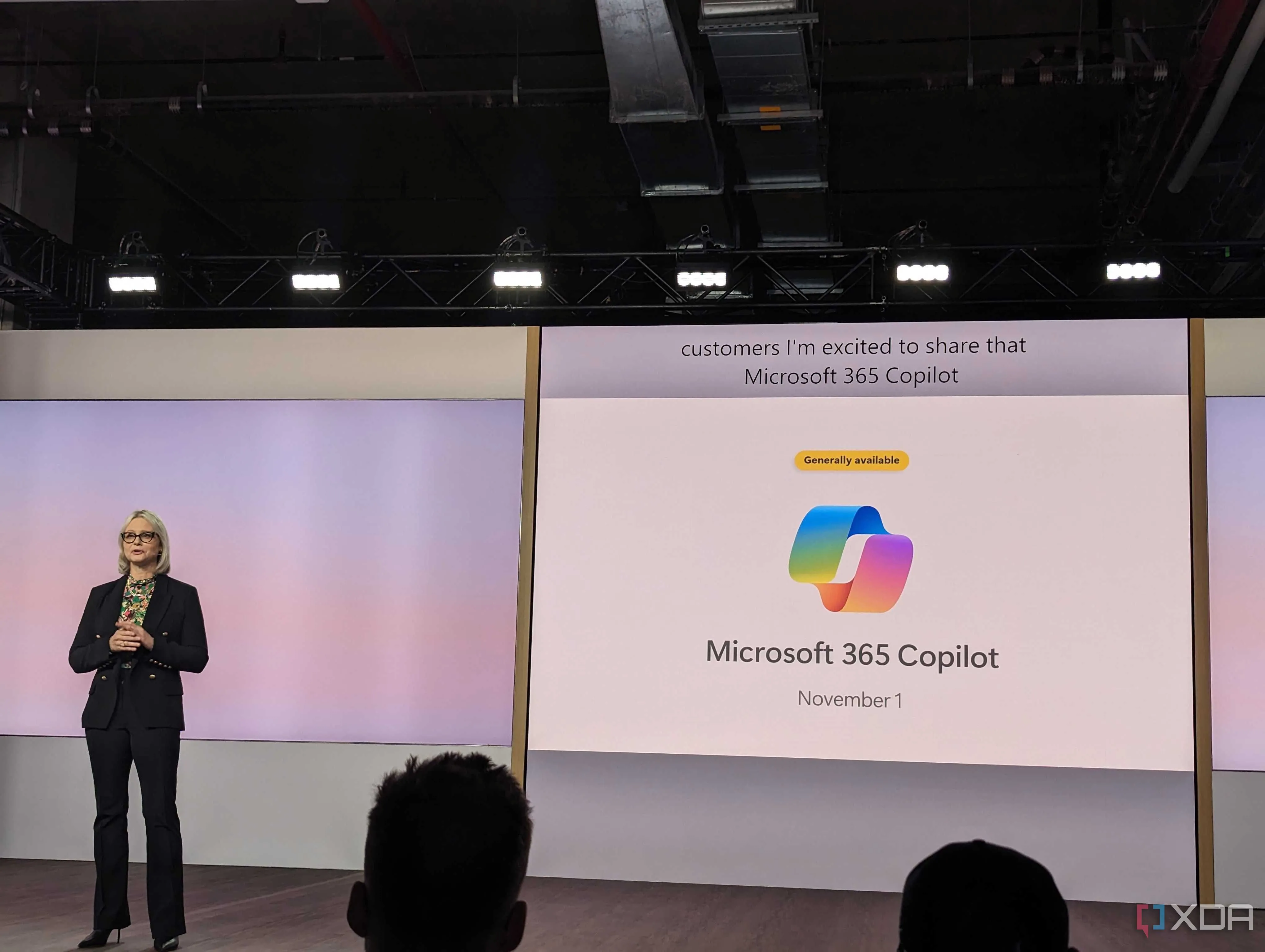 Logo Microsoft 365 Copilot được chiếu trên màn hình lớn phía sau sân khấu tại một sự kiện ra mắt sản phẩm của Microsoft.