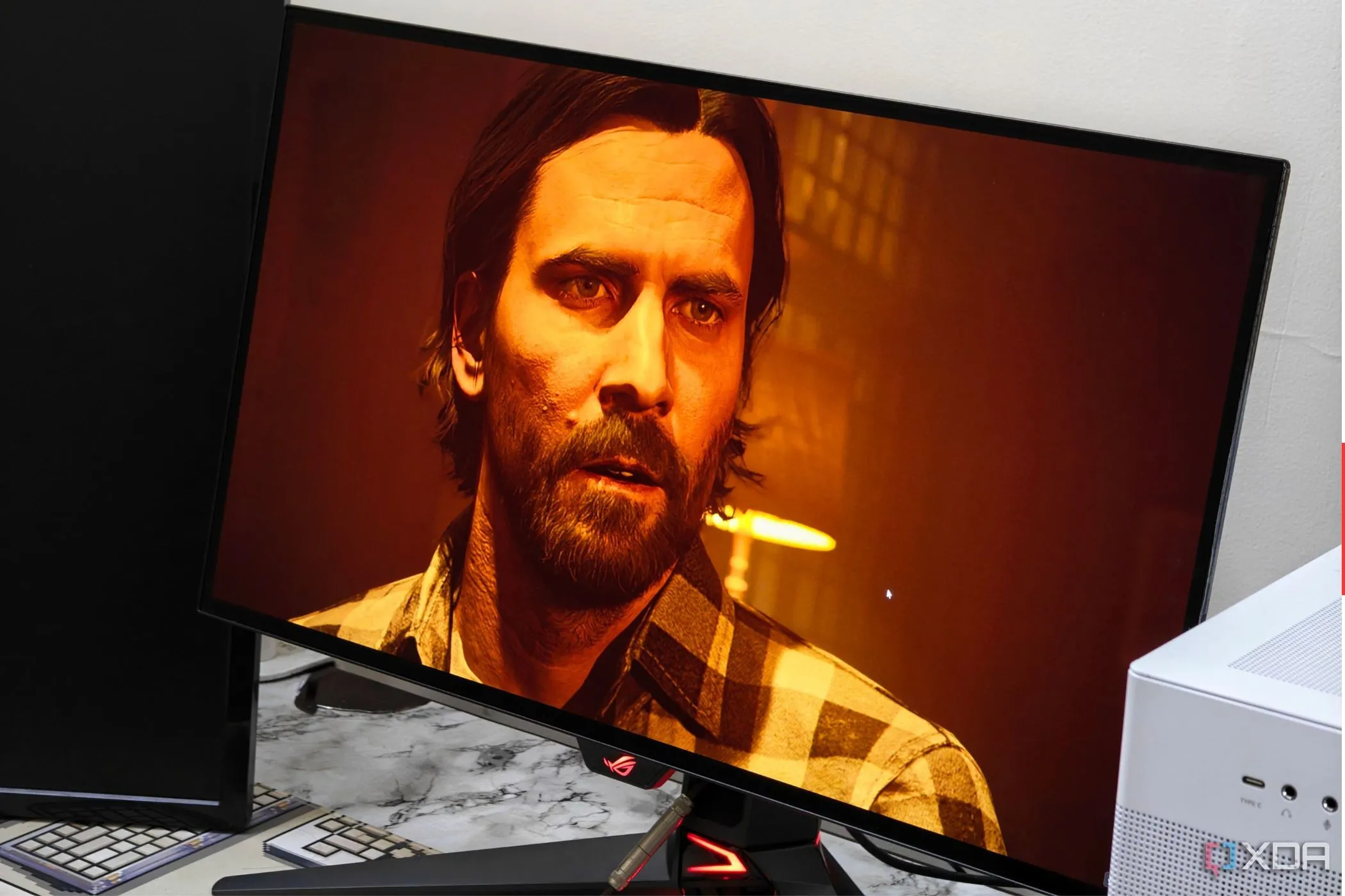 Màn hình Asus ROG Swift PG27AQDM hiển thị cảnh game Alan Wake 2 đang chạy, với đồ họa chân thực và hiệu ứng ánh sáng ấn tượng.
