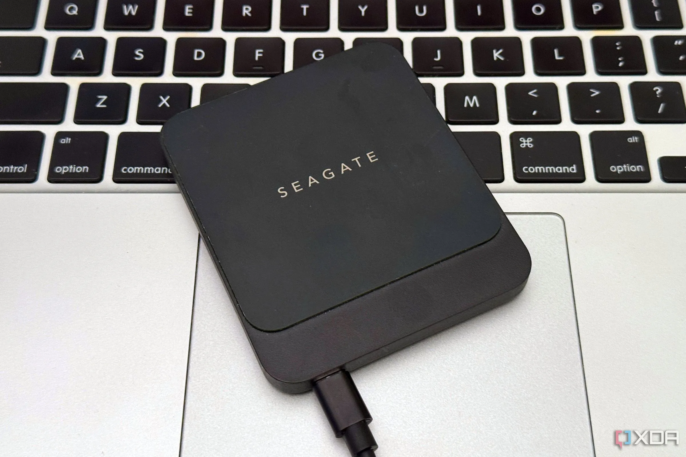 Một ổ cứng SSD di động được đặt trên bàn di chuột của MacBook, minh họa cho việc sử dụng thiết bị lưu trữ gắn ngoài để sao lưu và khôi phục dữ liệu.