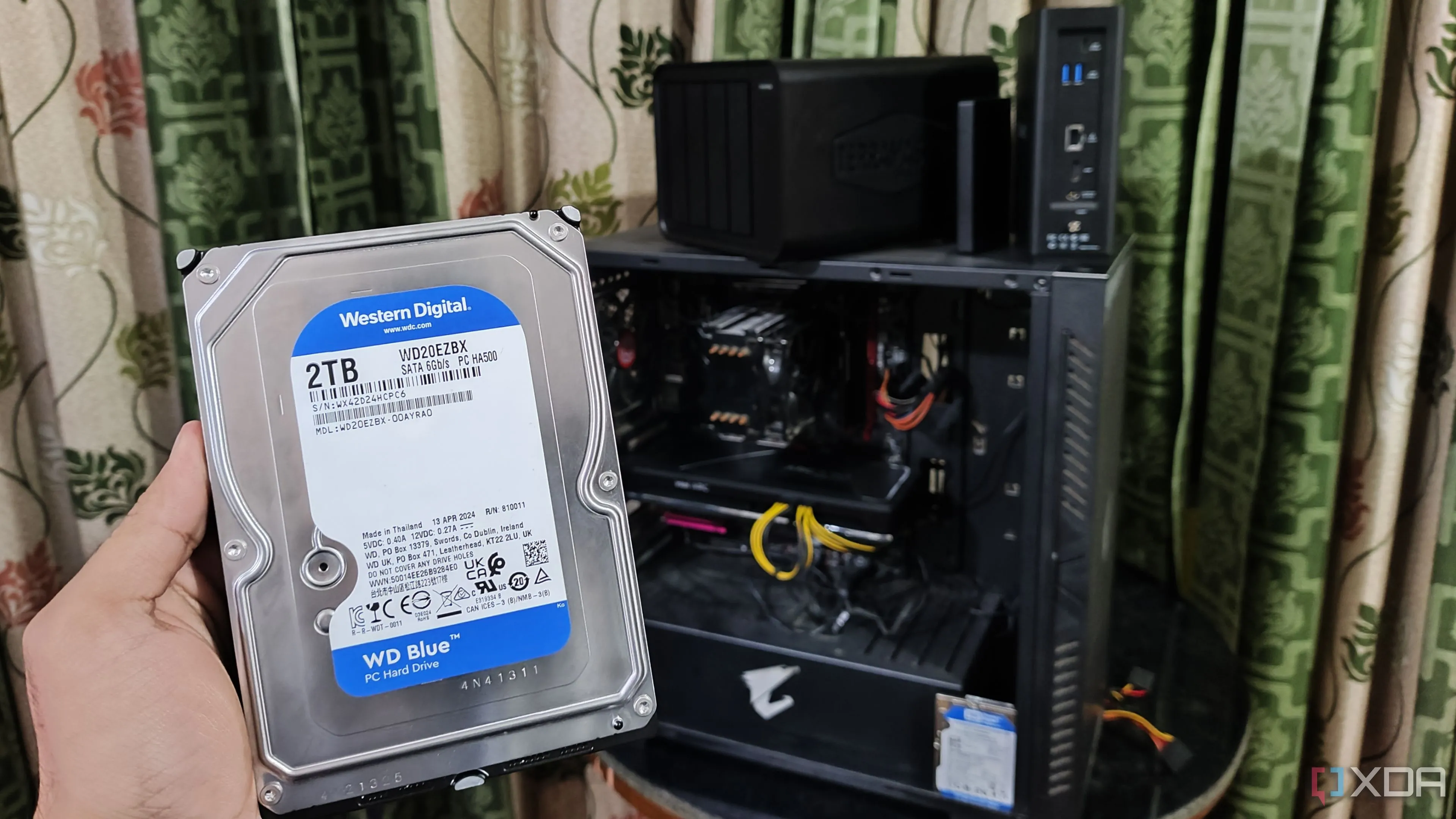 Người dùng đang cầm ổ cứng trước máy tính và hai thiết bị NAS TerraMaster